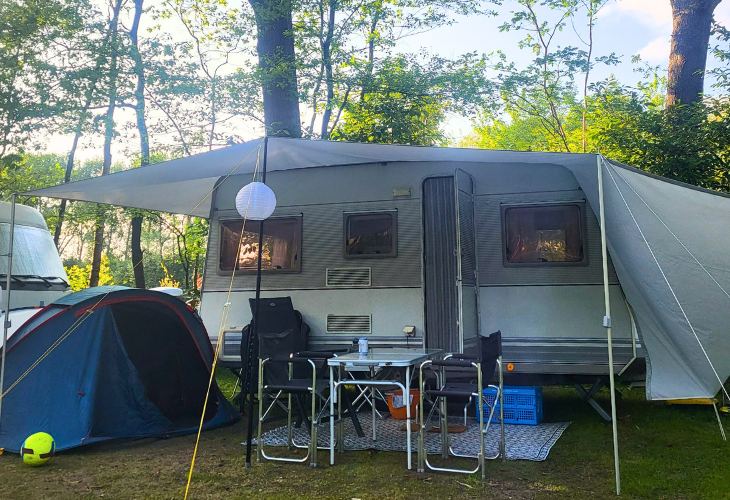 Caravan op camping met buitenkleed, luifel en kampeerstoelen ervoor, je ziet ook nog een bijzettentje van decathlon